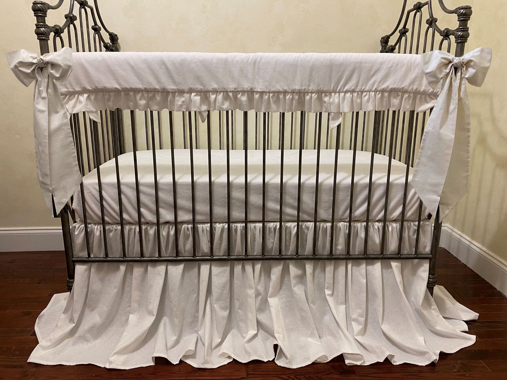 White crib with ruffled bedding in a room with striped wallpaper.
