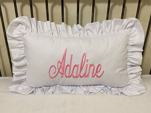 White pillow with ruffled edges and 'Adaline' embroidered in pink on a metal headboard.