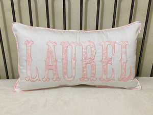 White pillow with pink embroidered text 'LAUREL' on a neutral background