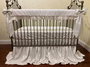 White crib with ruffled bedding in a room with striped wallpaper.