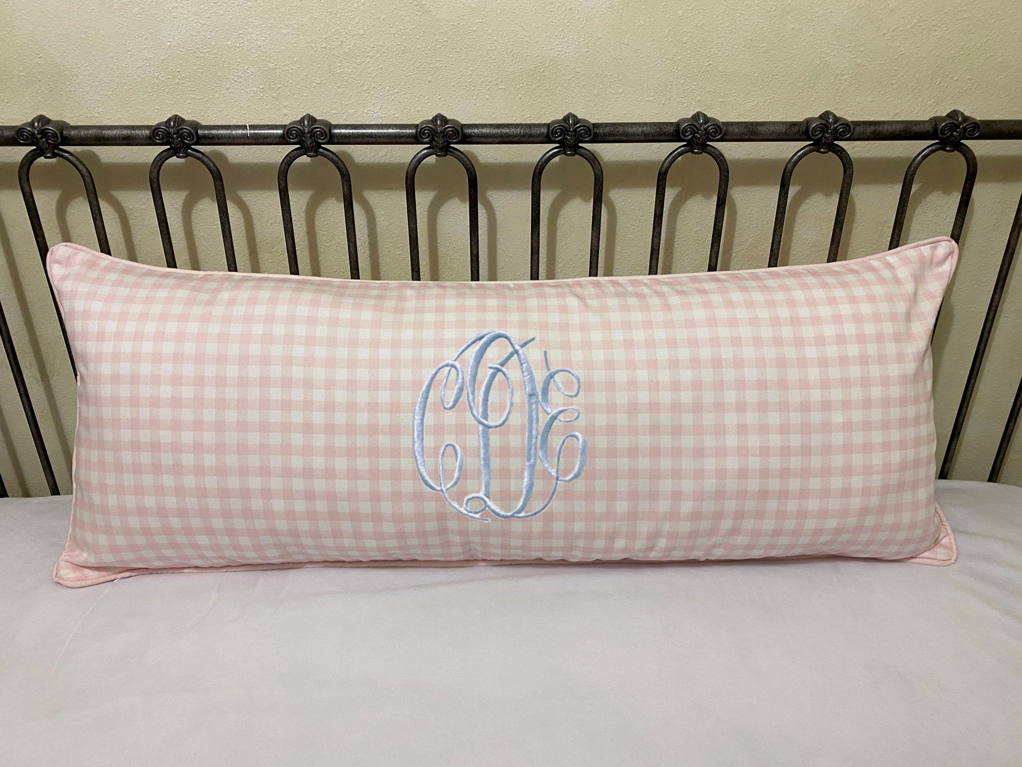 Pink checkered pillow with blue monogram on a bed